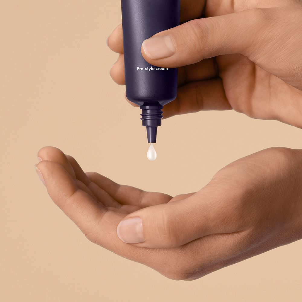 A drop of Dyson Chitosan Pre-style cream is squeezed into a hand from the 30ml mini bottle.
