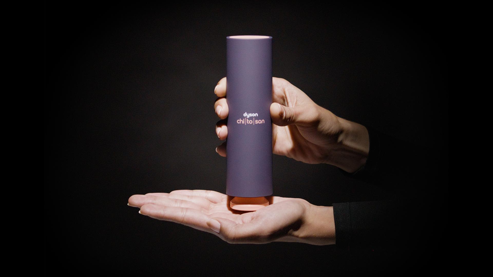 A hand holds a bottle of Dyson Chitosan Pre-style cream, with the pump positioned mid-palm.