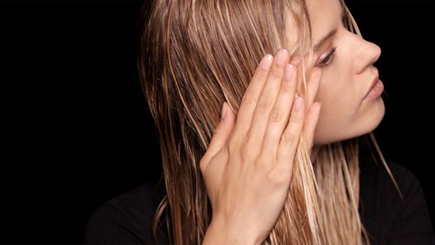 A model with long, damp hair uses her hands to smooth product through the lengths.