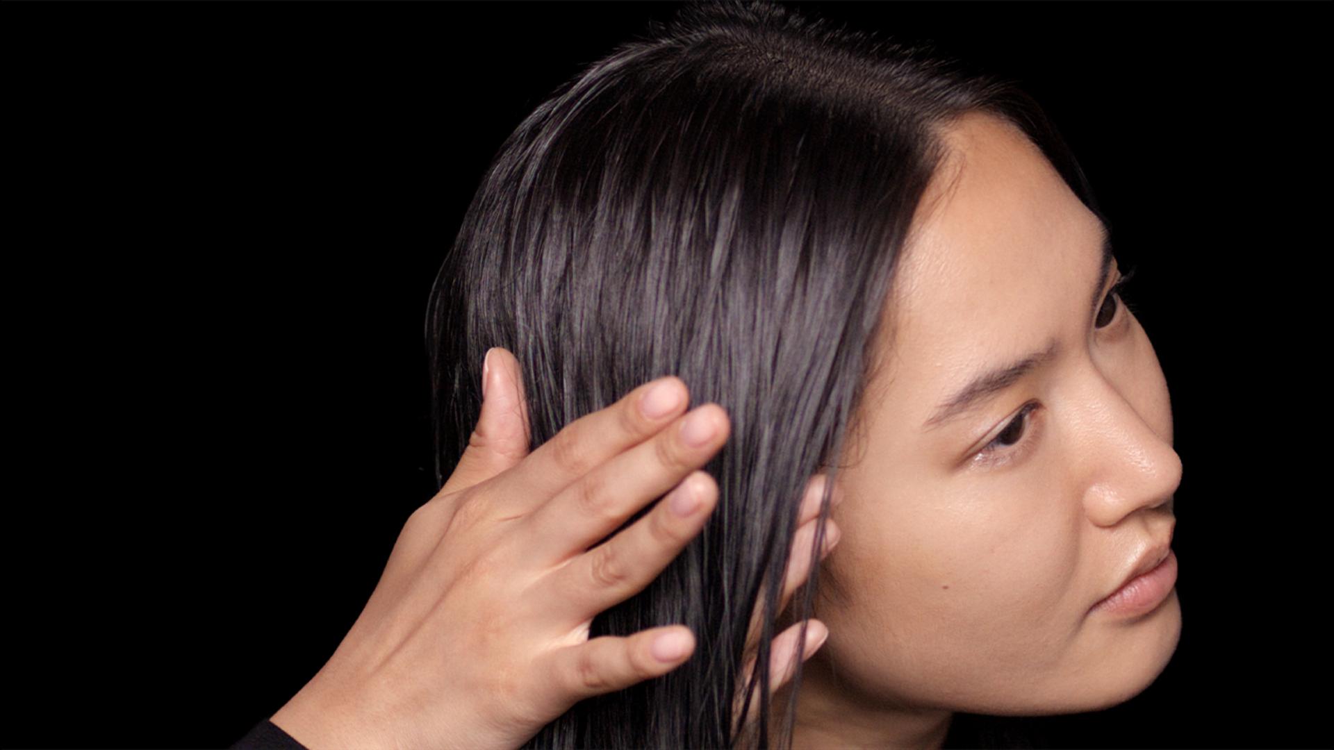 A model with long, damp hair uses her hands to smooth product through the lengths.