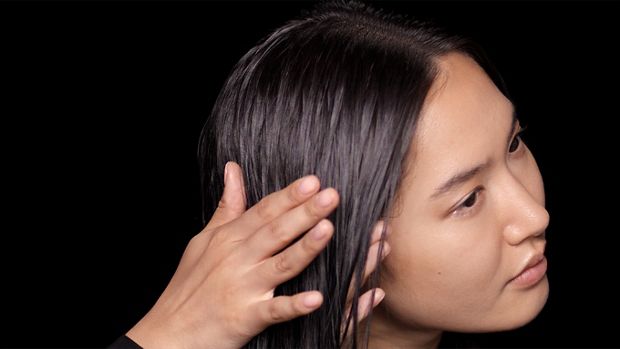 A model with long, damp hair uses her hands to smooth product through the lengths.