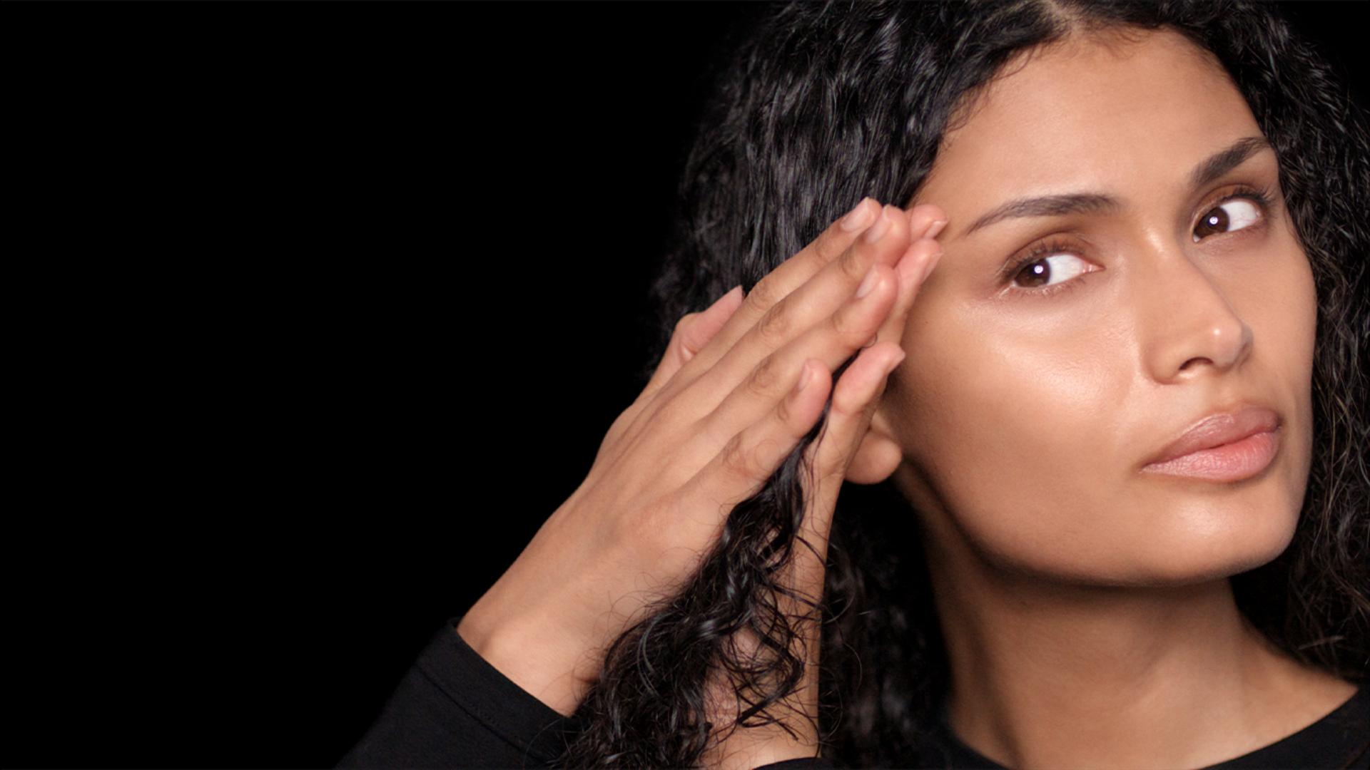 A model with long, damp hair uses her hands to smooth product through the lengths.