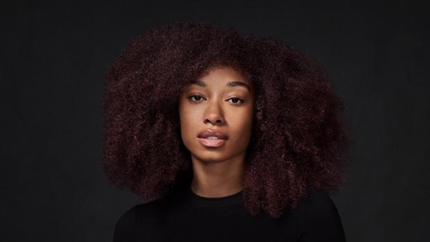 Model with long, coily, fine hair, against a dark background.
