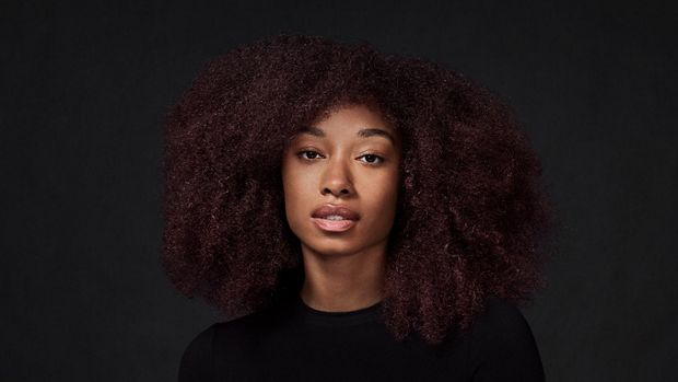 Model with long, coily, fine hair, against a dark background.