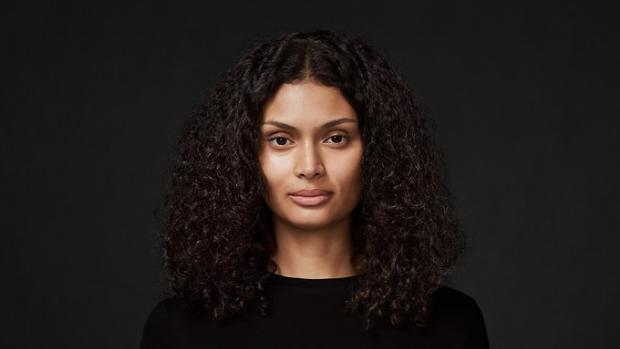 Model with long, curly, thick hair, against a dark background.