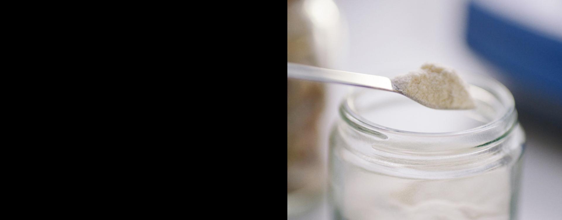 A spoonful of powdered ingredient being lifted from a glass jar.
