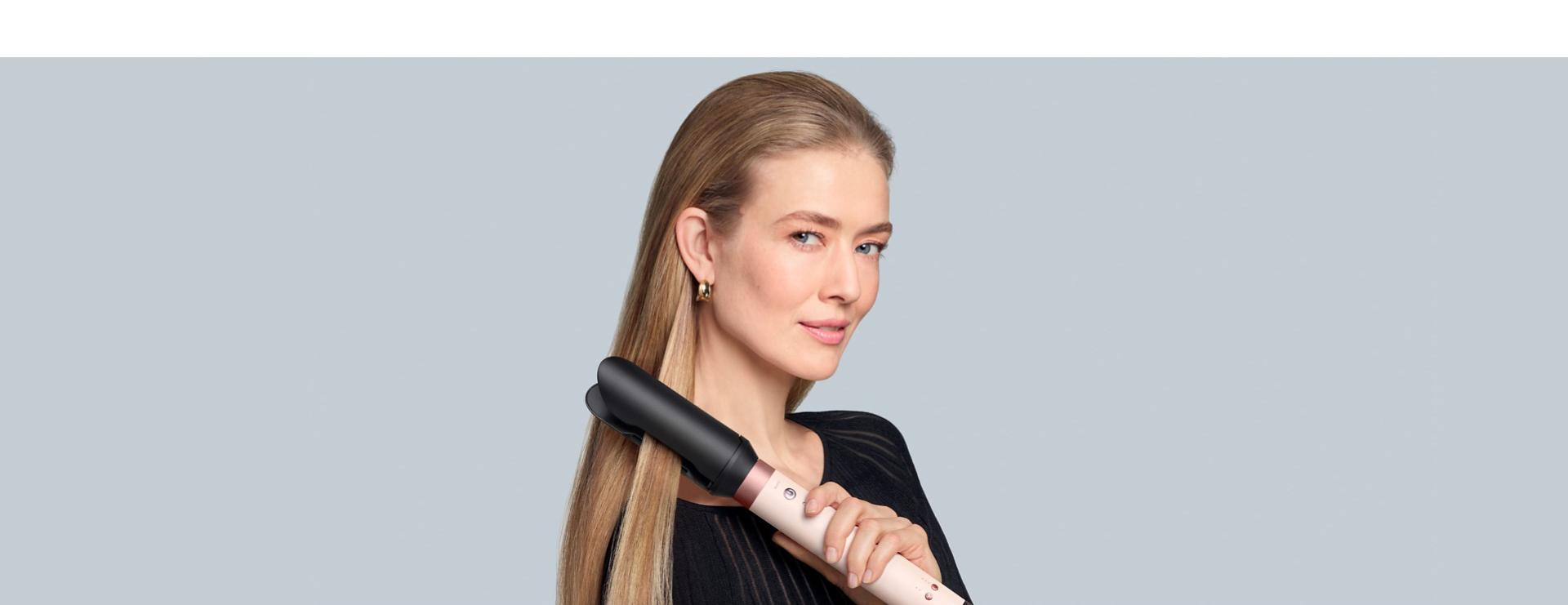 A blonde model straightens her hair using the Dyson Airwrap Co-anda2x multi-styler and dryer and the AirSmooth2x attachment.