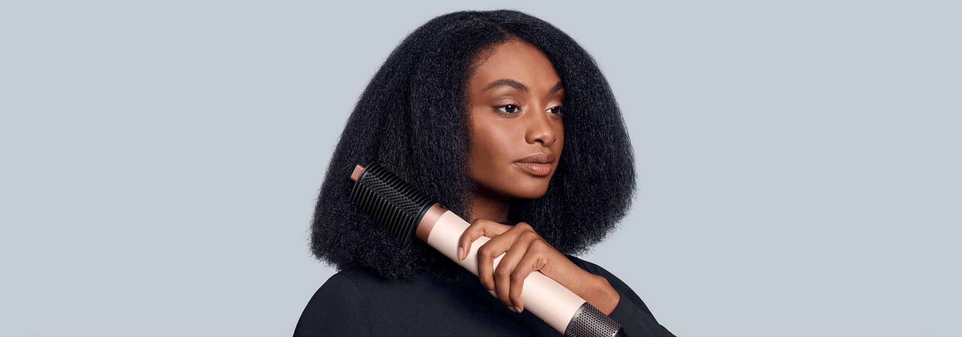 A model stretches her coily hair using the Dyson Airwrap Co-anda2x multi-styler and dryer and the Tension comb 2x.
