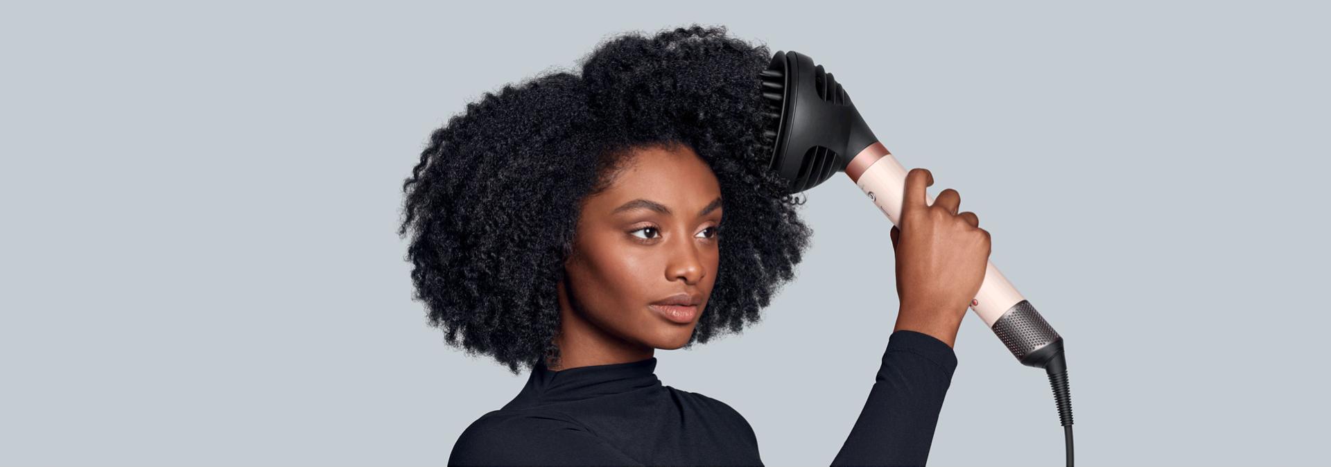 A model diffuses her coily hair using the Dyson Airwrap Co-anda2x multi-styler and dryer and the Wave+Curl diffuser 2x.
