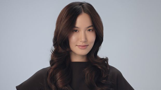 Một người mẫu với mái tóc đen được tạo kiểu thành những lọn xoăn mềm mại và bồng bềnh.