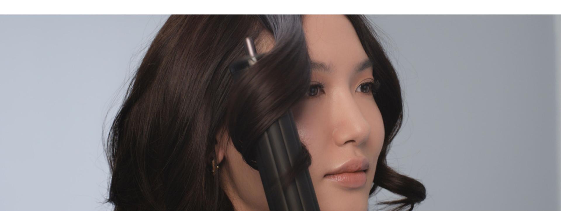 A model curls her dark hair using the Dyson Airwrap Co-anda2x multi-styler and dryer.