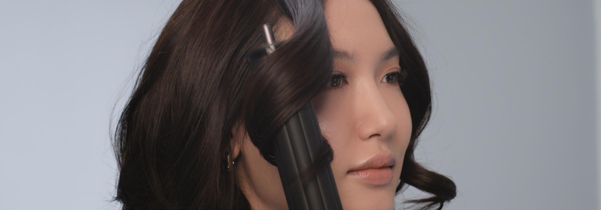 A model with dark hair curls her hair using the Dyson Airwrap Co-anda2x multi-styler and dryer.