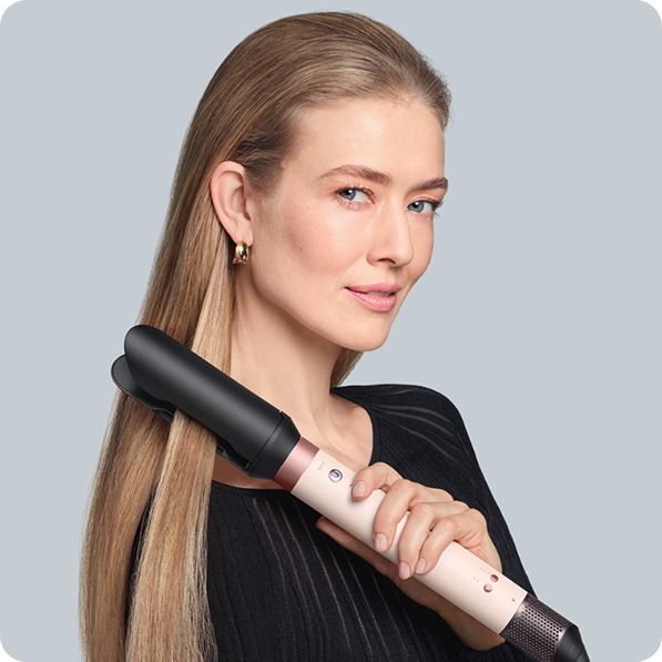 Egy szőke modell a Dyson Airwrap Co-anda2x multifunkciós készülékkel és az AirSmooth2x kiegészítővel egyenesíti a haját.