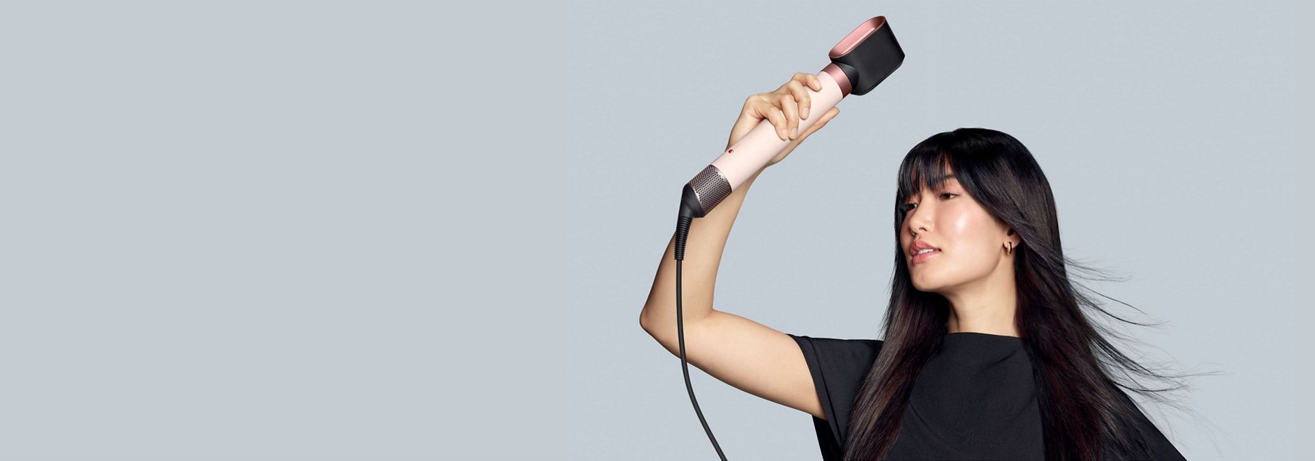 Egy sötét hajú modell a Dyson Airwrap Co-anda2x multifunkciós hajformázó-szárítót és a Gyorsszárító 2x kiegészítőt használja hosszú hajának szárítására.