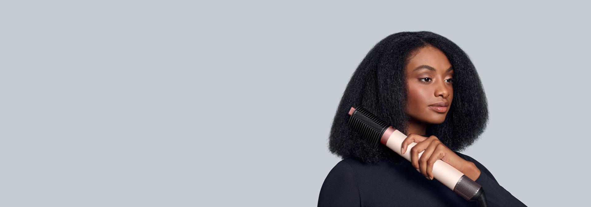 The Dyson Airwrap Co-anda2x multi-styler and dryer with the Tension Comb 2x attachment used by a model.
