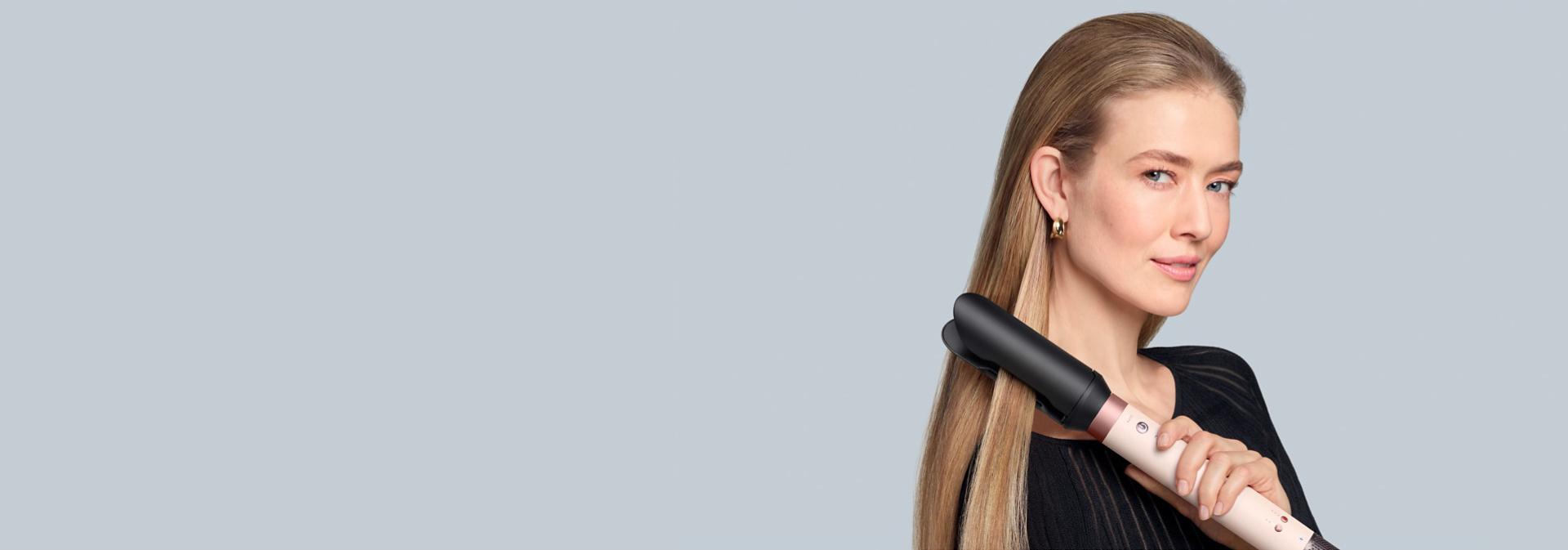 A blonde model straightens her hair using the Dyson Co-anda2x multi-styler and dryer and the AirSmooth2x attachment.