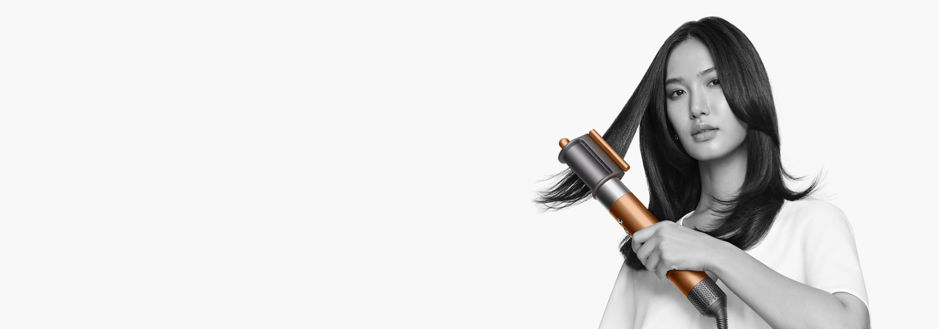 다이슨 에어랩 오리진 멀티 스타일러 앤 드라이어로 잔머리를 매끄럽게 스타일링하는 갈색 모델.