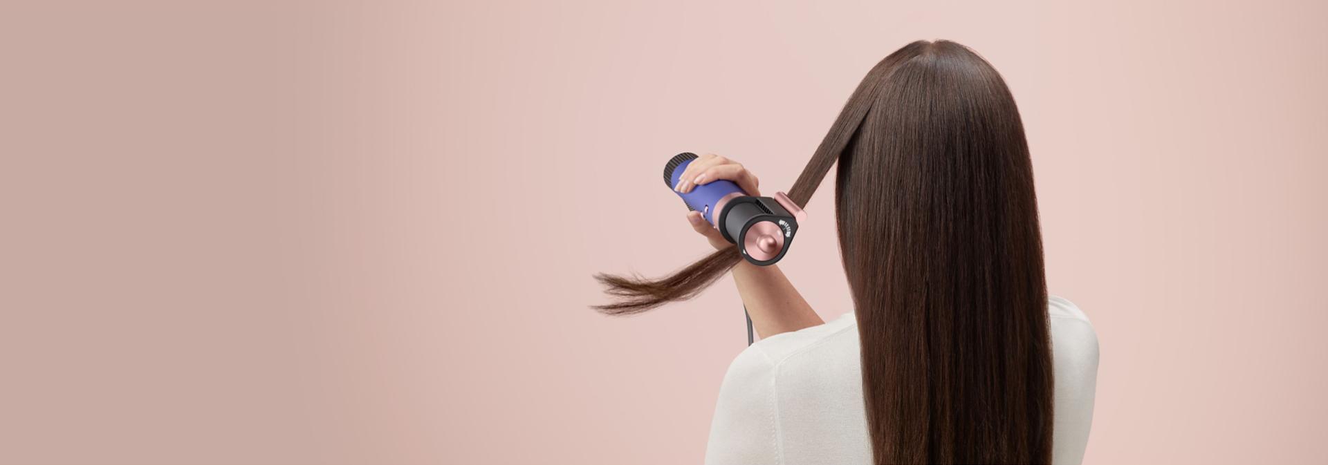 A brunette model smooths flyaways with her Dyson Airwrap Origin multi-styler and dryer.