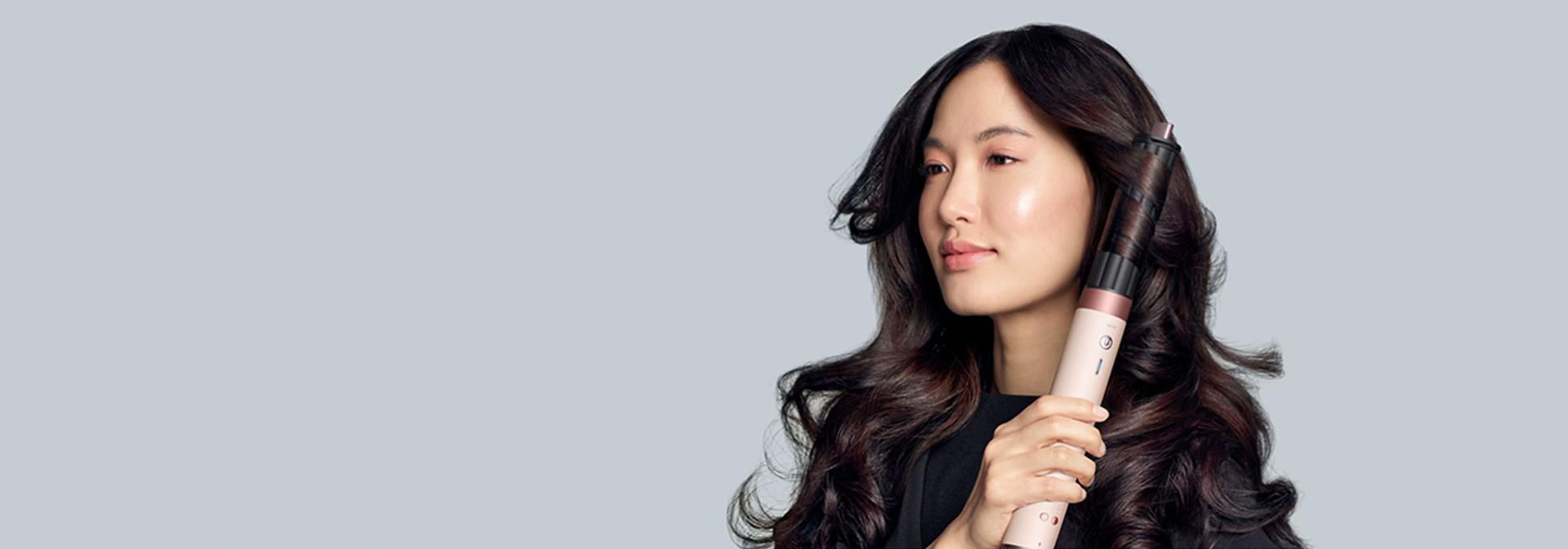 A model with dark hair adds curls using the Dyson Airwrap Co-anda2x multi-styler and dryer.