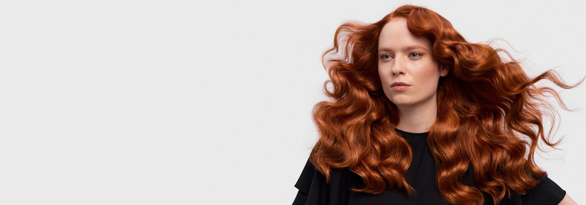 Modelka z długimi, falowanymi i rudymi włosami prezentuje efekt uzyskany dzięki multistylerowi i suszarce Dyson Airwrap i.d.