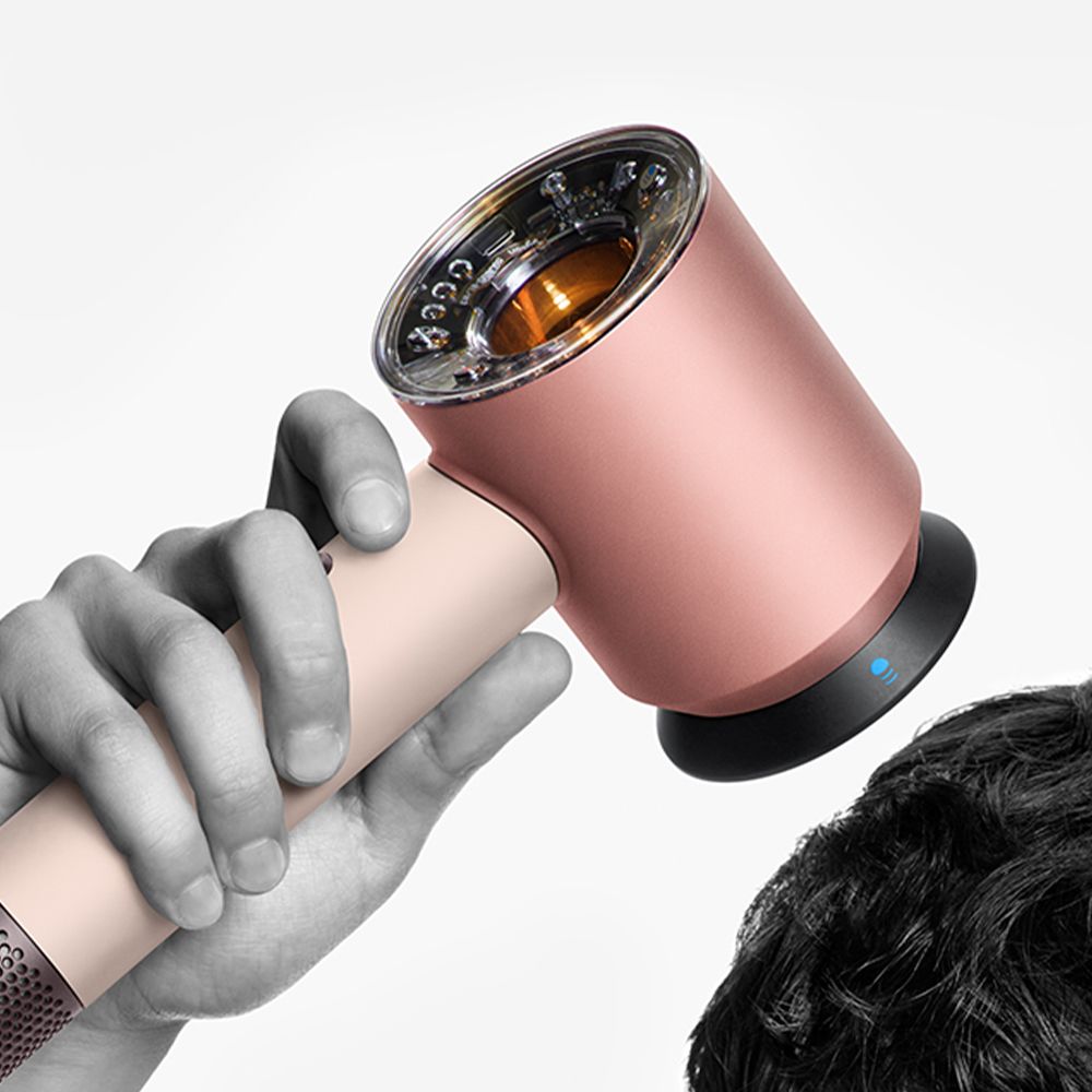 A model styles her hair with the Dyson Supersonic Nural hair dryer and Wave+Curl diffuser.