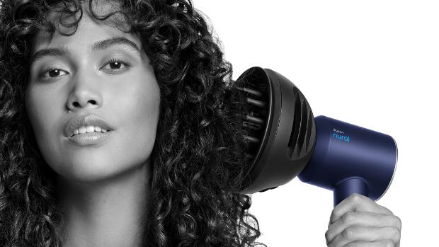 Kıvırcık saçlarına Dyson Dalga+Bukle difüzörüyle hacim kazandıran bir kadının yakın çekimi.