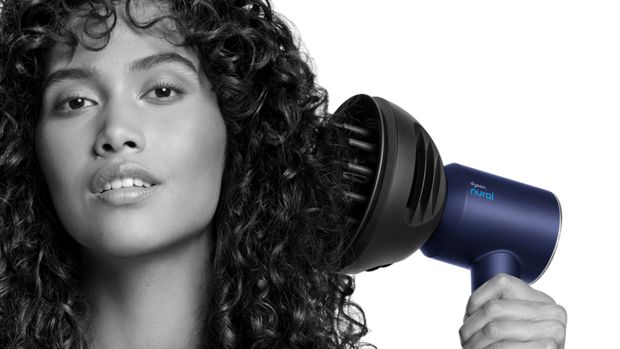 Kıvırcık saçlarına Dyson Dalga+Bukle difüzörüyle hacim kazandıran bir kadının yakın çekimi.