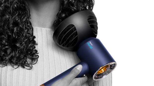 Kıvırcık saçlarının uçlarını Dyson Dalga+Bukle difüzörüyle kurutan bir kadının yakın çekimi.