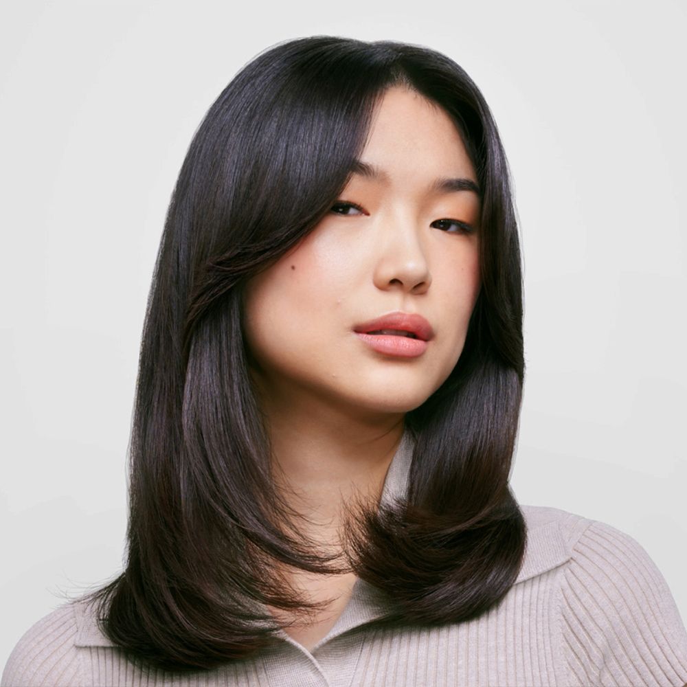 Model with long dark hair styled with the Dyson Supersonic Nural hair dryer.