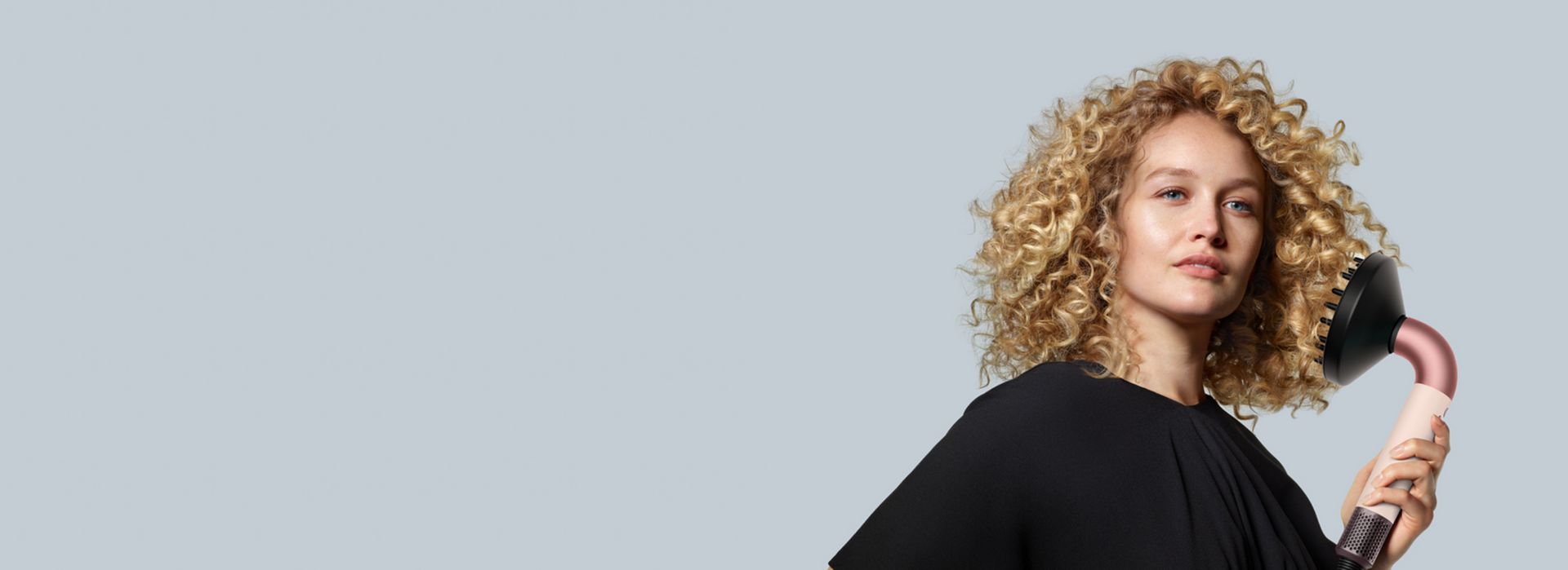 The Dyson Supersonic r with Diffuser attachment is held by a model with blonde curly hair.