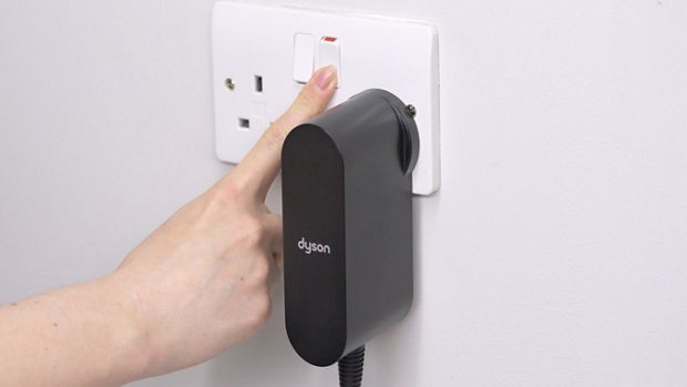 The plug of the Dyson Supersonic r hair dryer is plugged into a wall outlet and switched on.