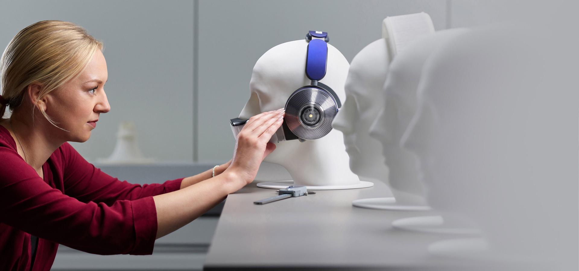 Woman placing Dyson Zone noise-cancelling headphones onto dummy's head