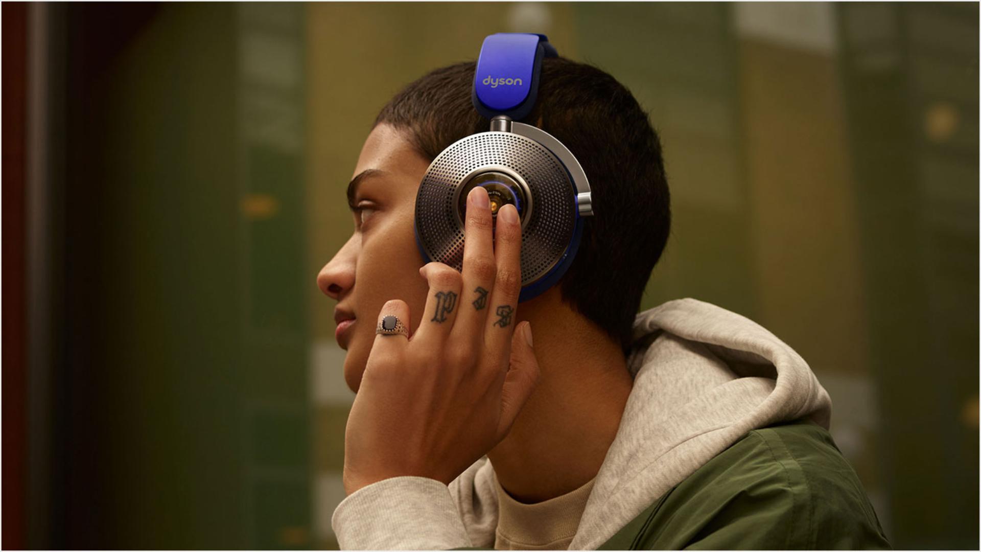 Woman wearing Dyson zone noise-cancelling headphones. She taps the back of the left ear cup.