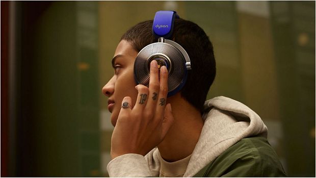 Woman wearing Dyson zone noise-cancelling headphones. She taps the back of the left ear cup.