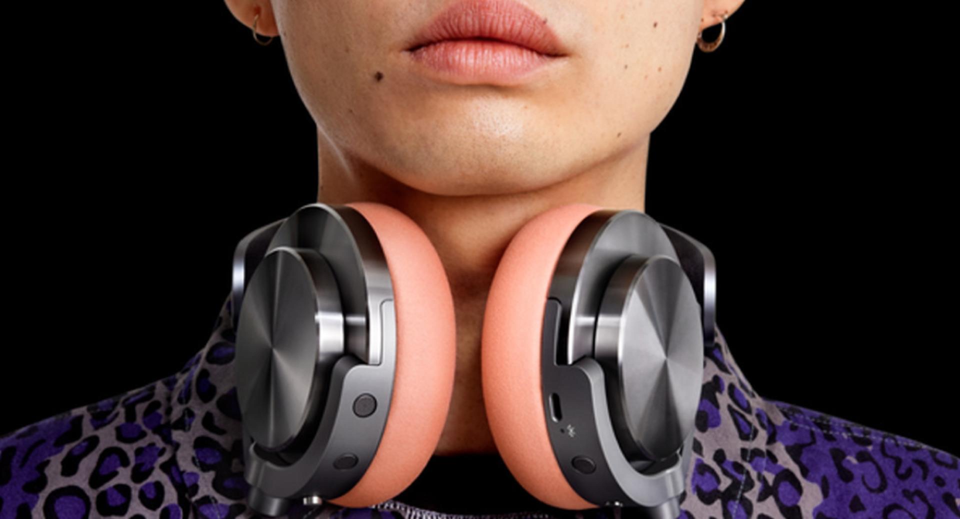 Metalik gri dış kapaklı ve açık pembe kulaklık yastıklı Dyson OnTrac™ kulaklığı boynuna takmış bir model.