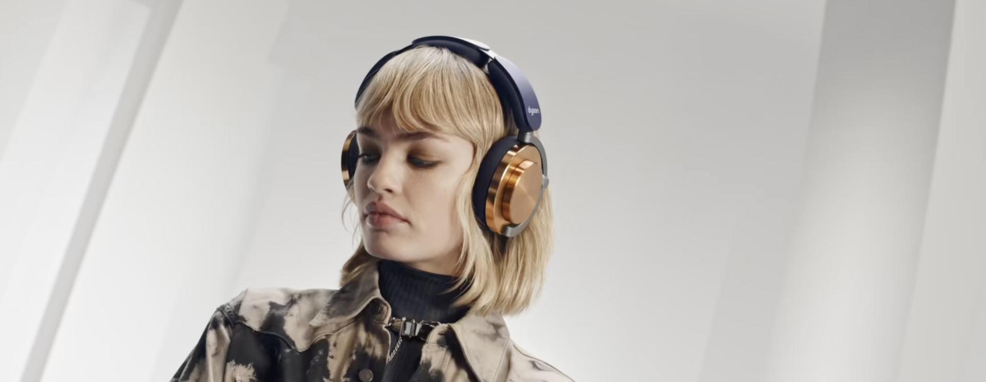 Blonda modele, kas skatās uz leju, valkājot Dyson OnTrac austiņas ar CNC vara krāsas kausiņiem.