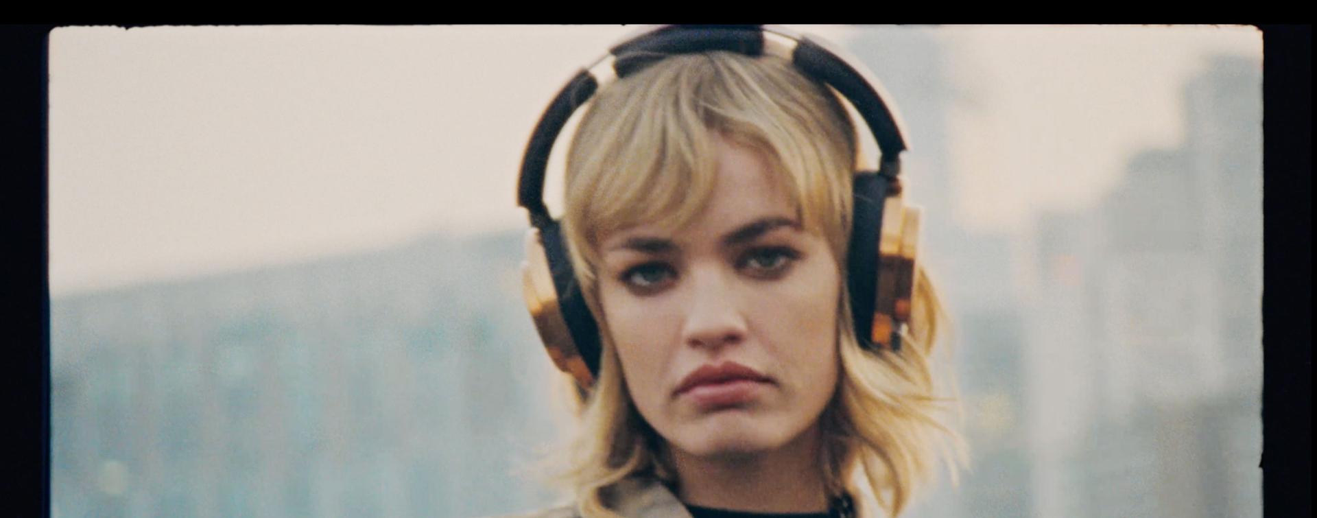 Blonda modele valkā Dyson OnTrac austiņas ar CNC vara krāsas kausiņiem.