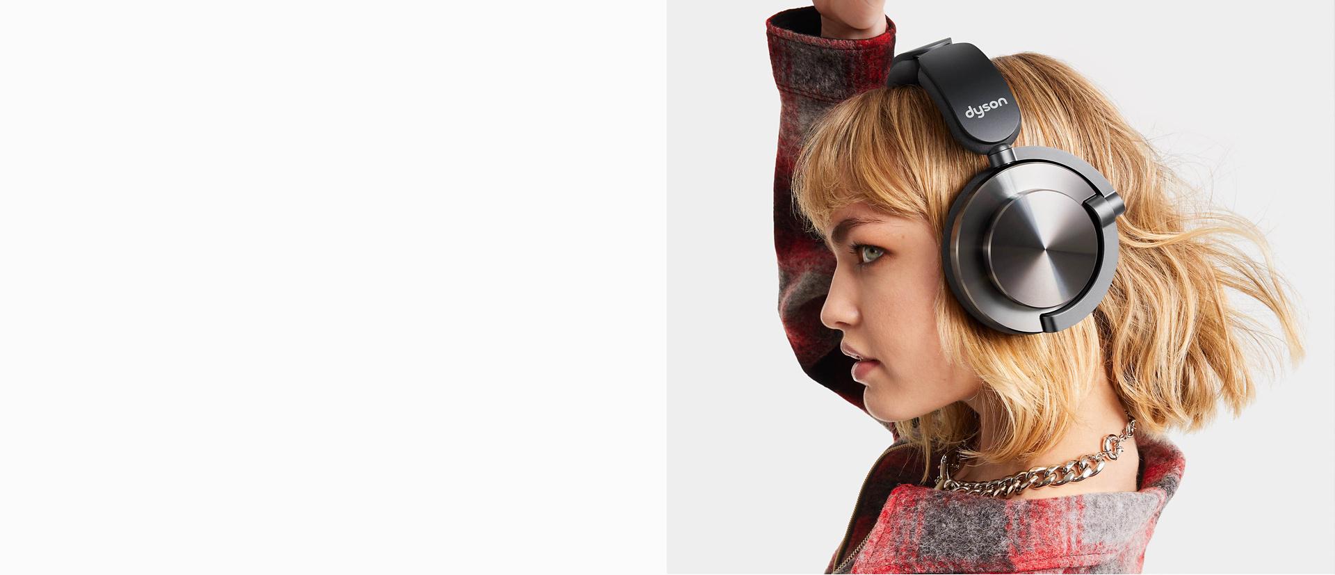 CNC 알루미늄 캡이 장착된 다이슨 온트랙 헤드폰을 착용하고 손을 머리 위로 올린 모델의 옆모습.