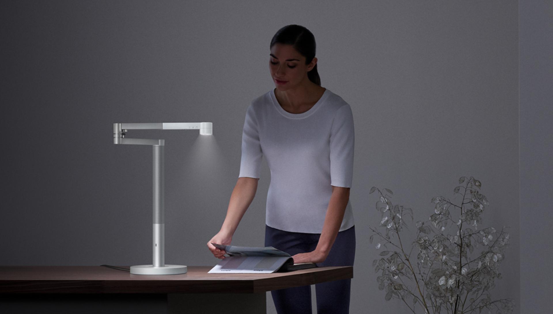 Dyson Lightcycle Morph lambanın parlak ışığı altında kağıtlara bakan kadın