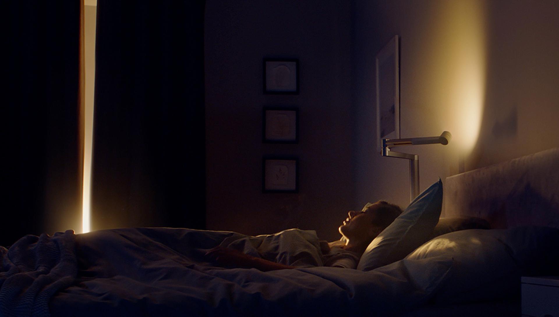 Woman waking up to the soft morning glow of a Dyson Lightcycle Morph lamp