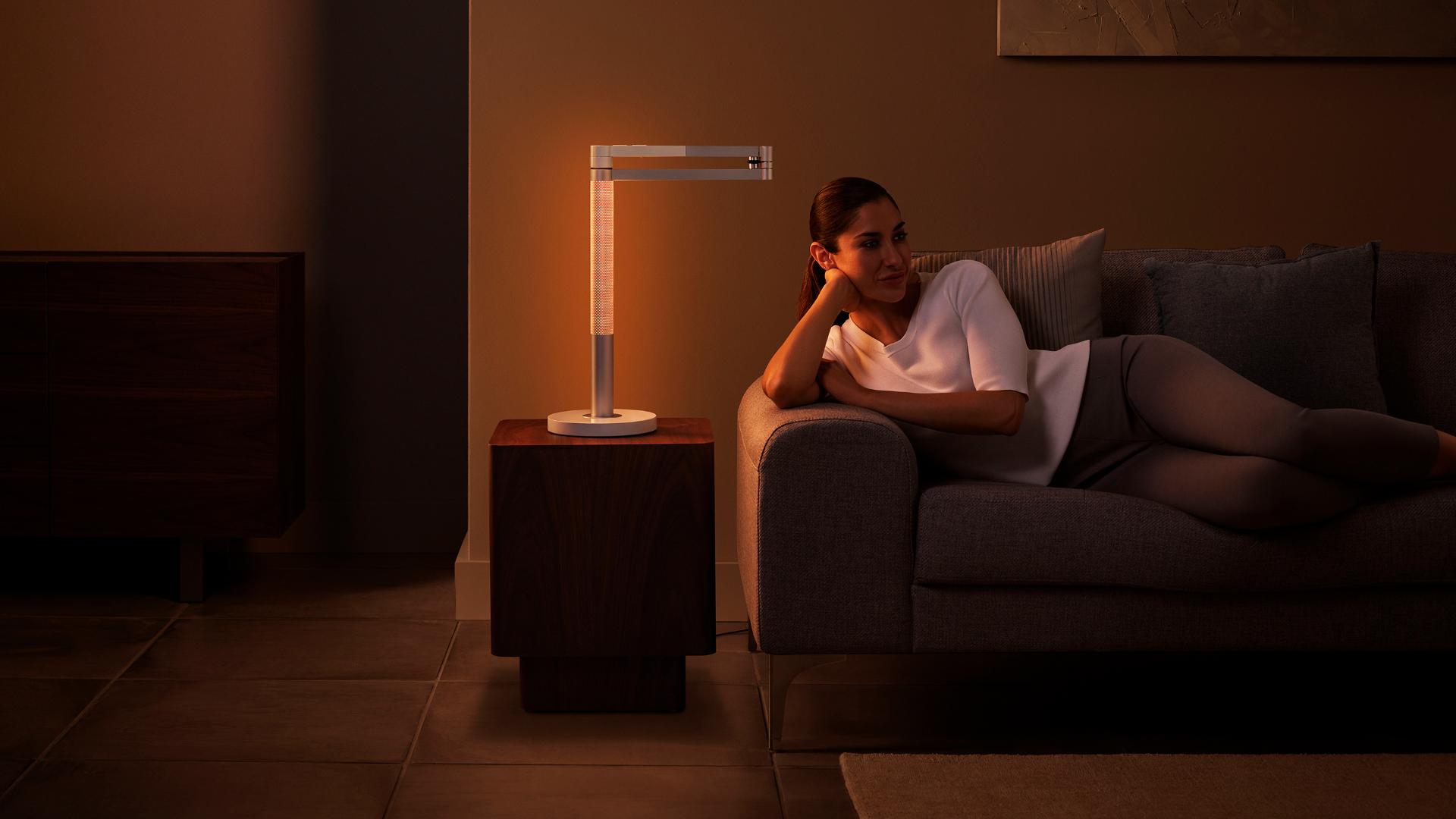 Woman basking in a orange ambient glow from the Dyson Lightcycle Morph light