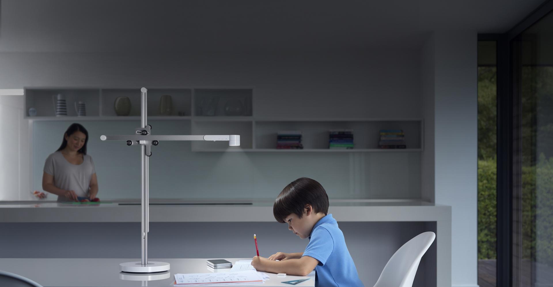 Boy studying at desk under powerful Dyson Lightcycle task light with mother in the background
