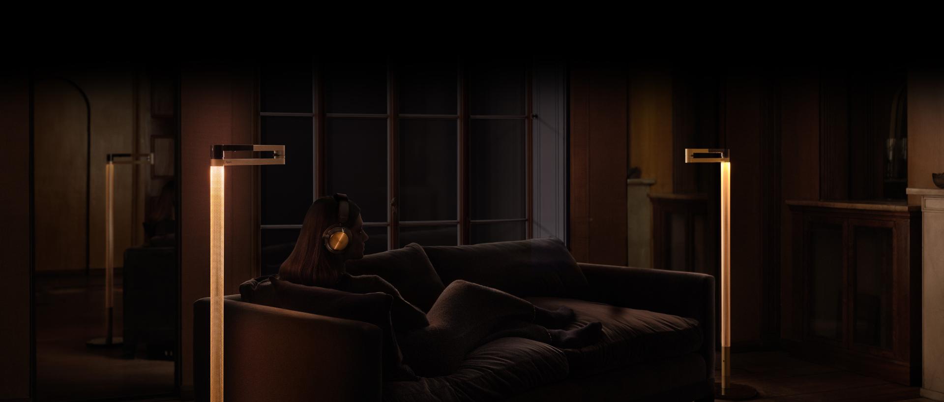 Propietario de los audífonos Dyson OnTrac sentado en el sofá con la lámpara de pie Dyson Solarcycle Morph.