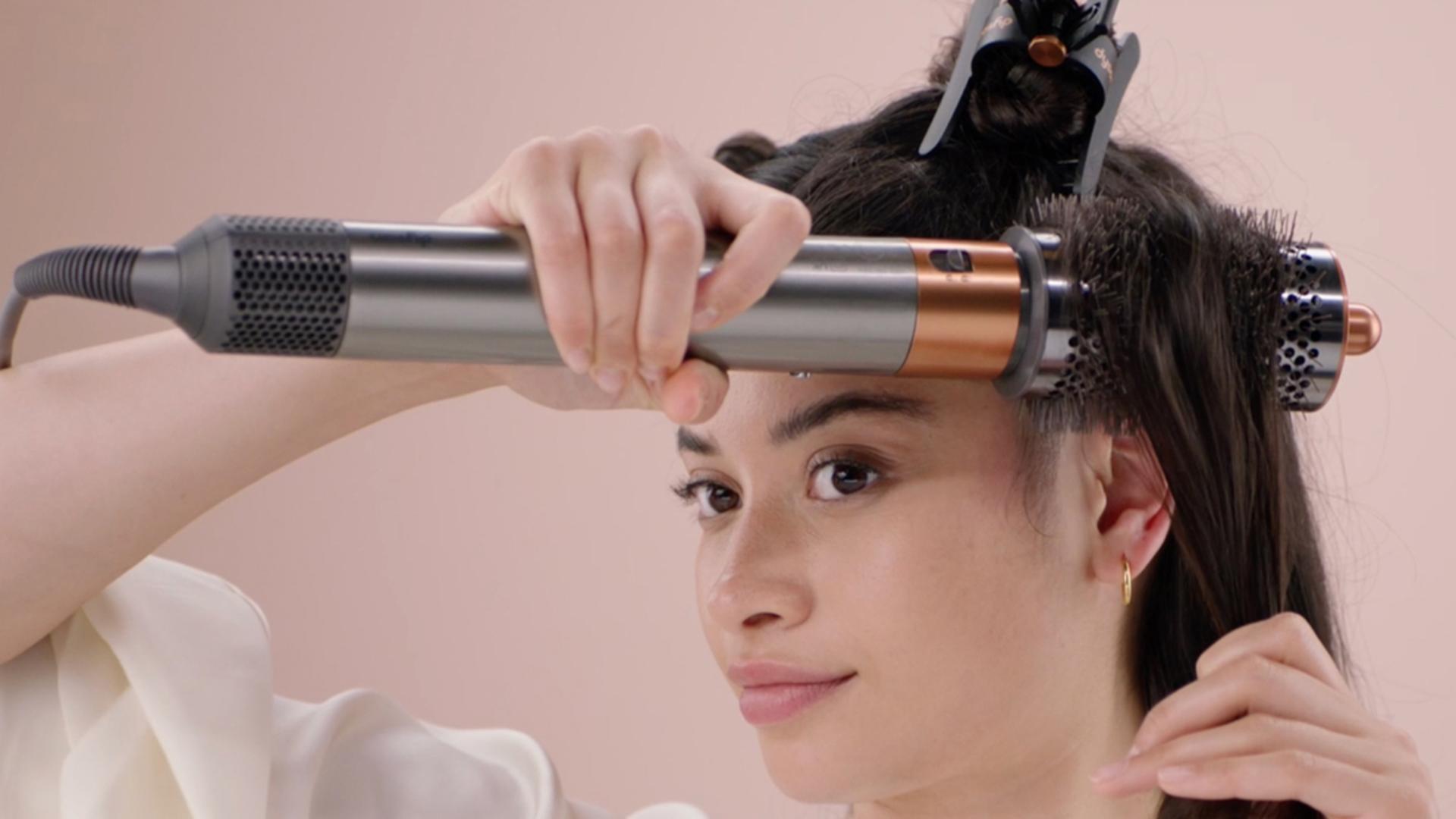 A model styling their hair with the Dyson Large round volumising brush.