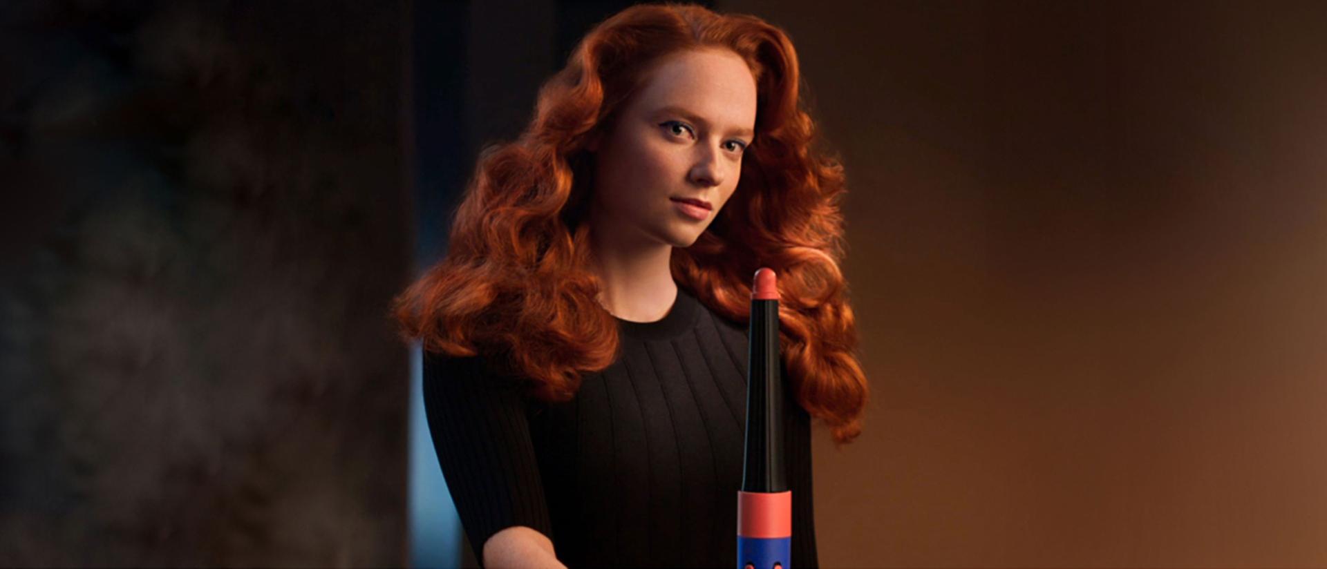A redheaded model with loose curls styled with the Dyson Airwrap i.d. curl mode.