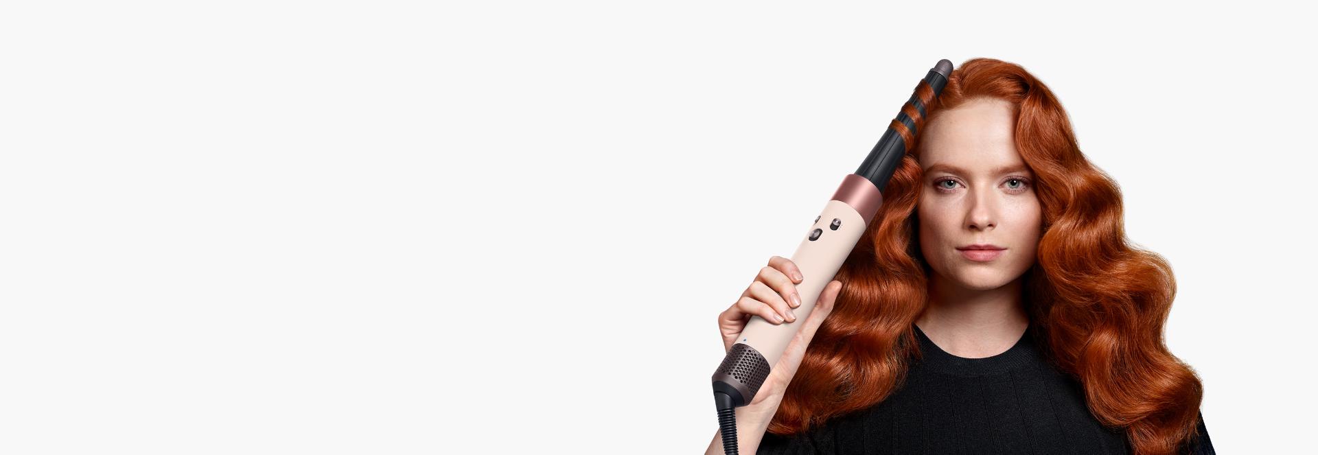 A redhead model with long hair uses the Conical Airwrap barrel to add waves to her hair.