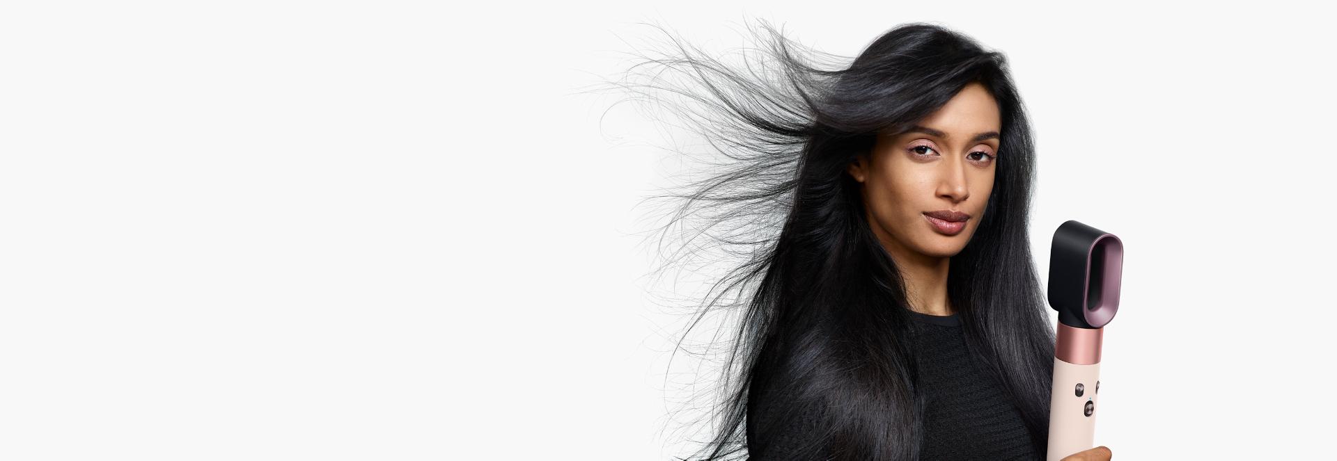 A model with long, dark hair uses the Fast dryer attachment to rough dry her hair.