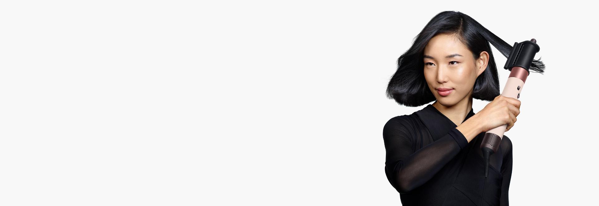 A model with medium length black hair uses the Dryer+Flyaway smoother attachment to smooth her hair style.