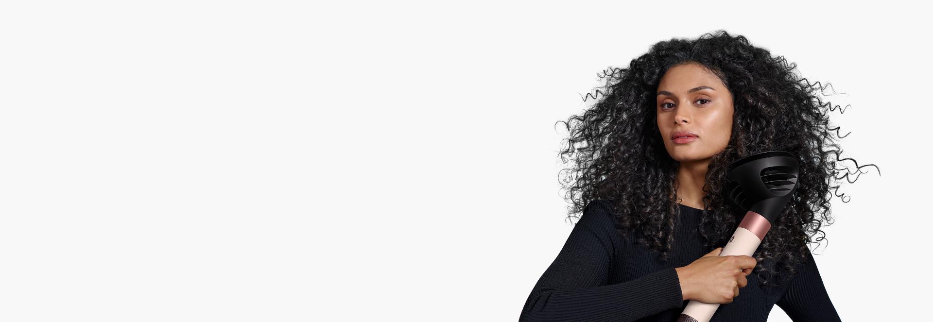 Un model cu părul închis la culoare folosește difuzorul Wave+Curl pentru a-și perfecționa buclele naturale.