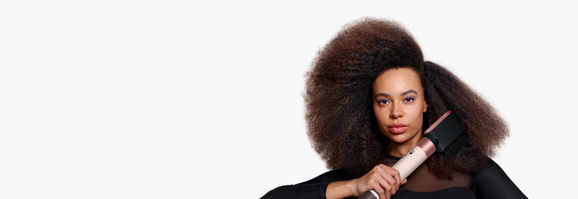 Un model cu părul afro folosește accesoriul pieptene cu dinți rari pentru a-și modela și întinde părul natural.